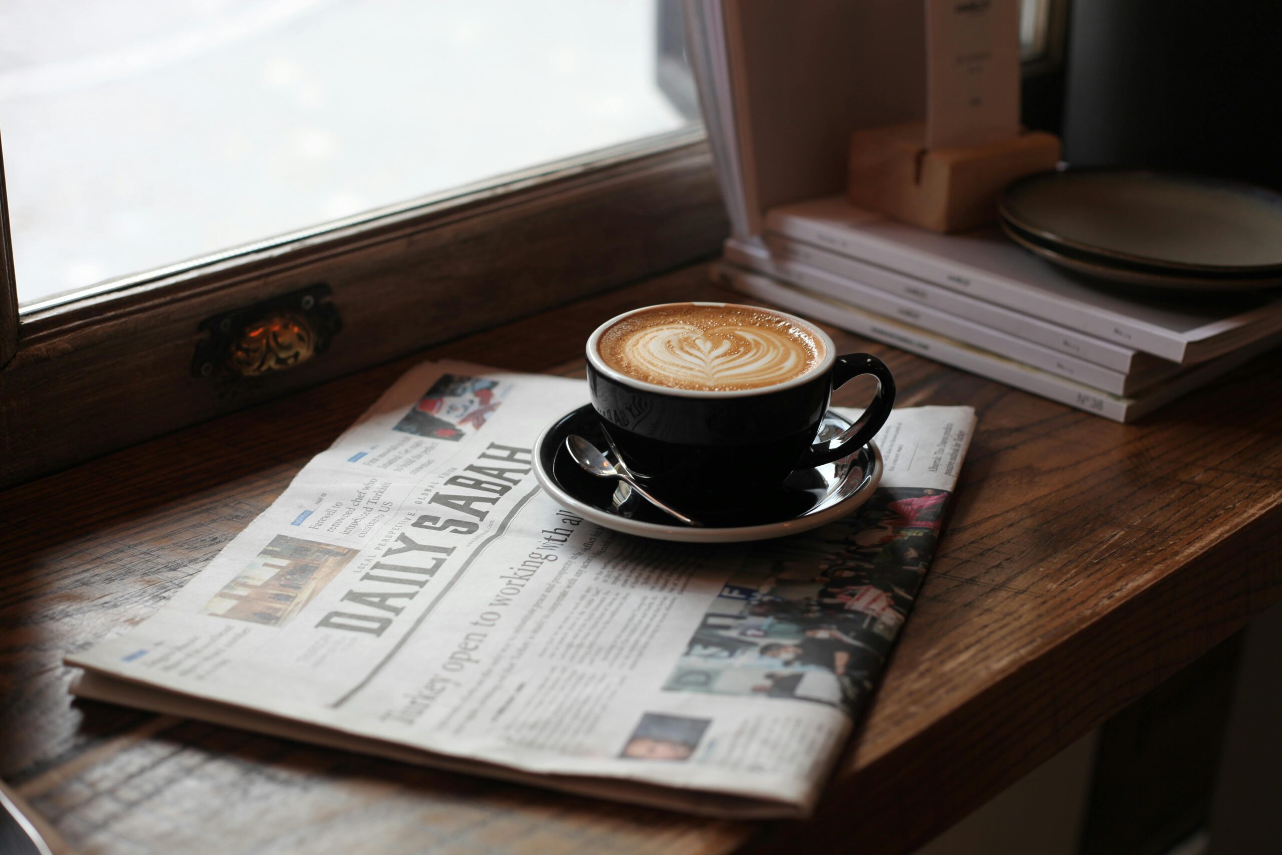 A warm café atmosphere in Istanbul featuring a latte with art sitting on a newspaper by the window.